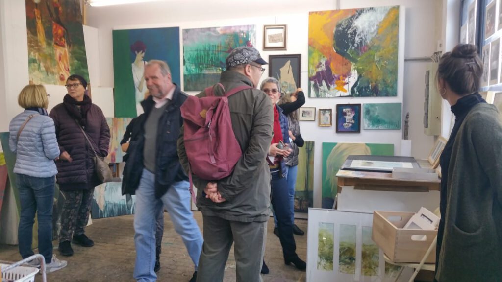 Mehrere Menschen stehen in einem Atelier mit Kunstwerken an den Wänden