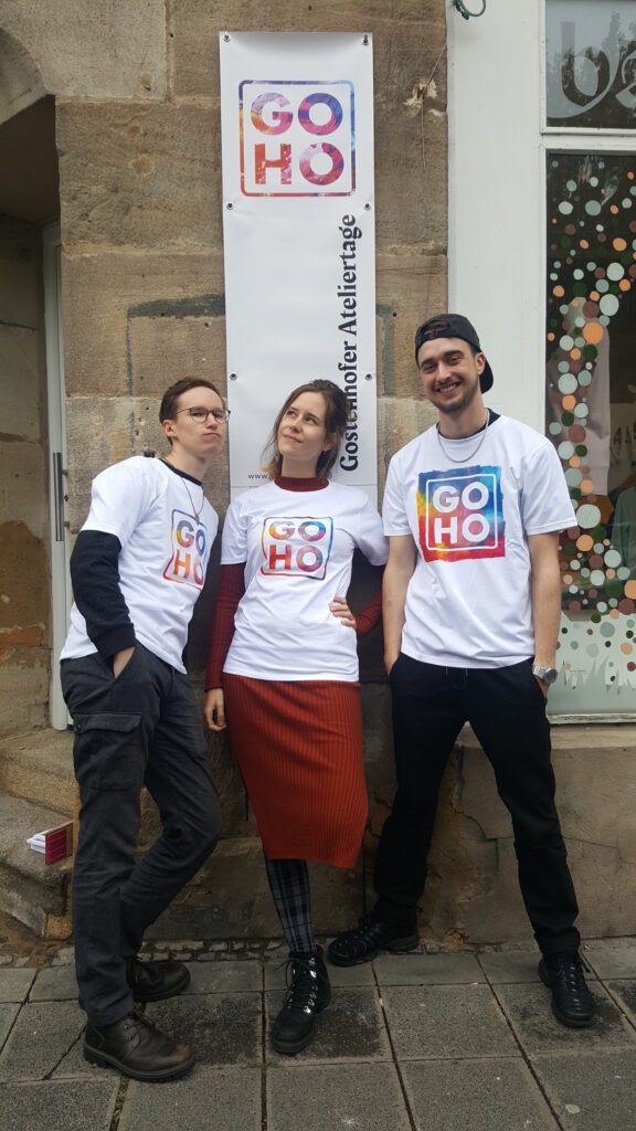 drei junge Menschen mit GOHO-shirt posieren vor einem Ladeneingang